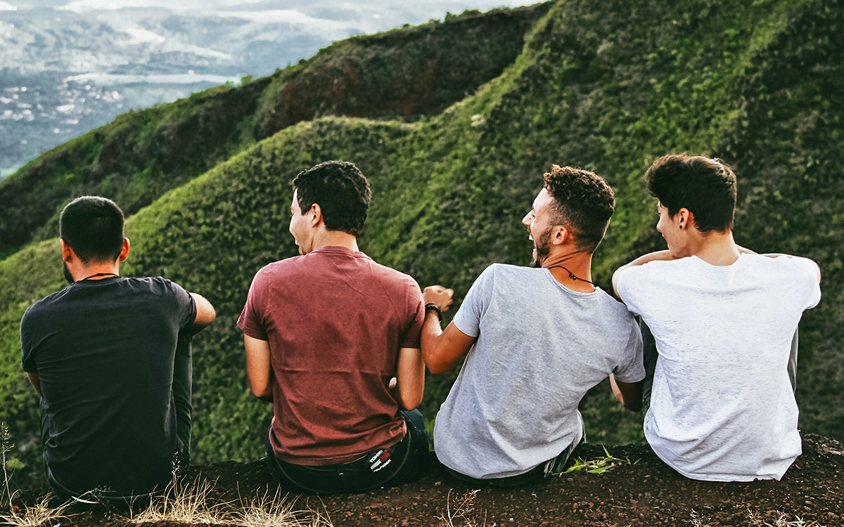 Four young men sitting on a wall with a view over hills and valley